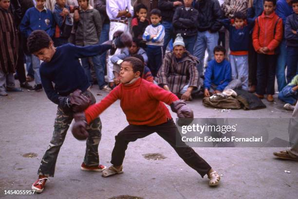 As a large crowd watches, two young boys, both in padded gloves, box in Jemaa El-Fnaa square, Marrakech, Morocco, March 5, 1989.