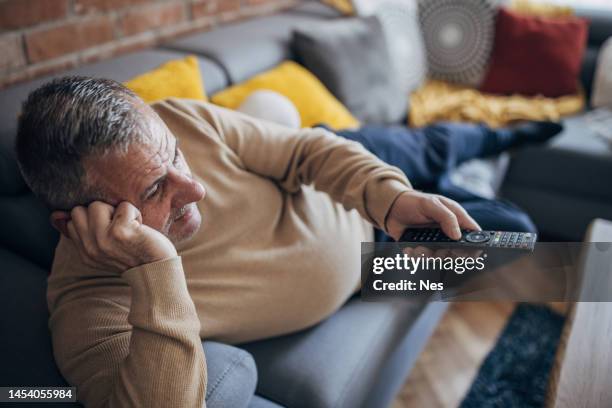 ein dicker mann liegt auf einem sofa und hält eine tv-fernbedienung in der hand - magen eines menschen stock-fotos und bilder