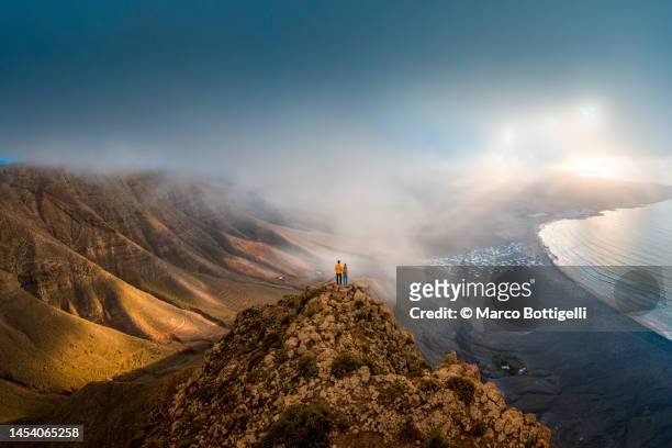 couple standing on top of a cliff looking at sunset, lanzarote, spain - travel stock-fotos und bilder