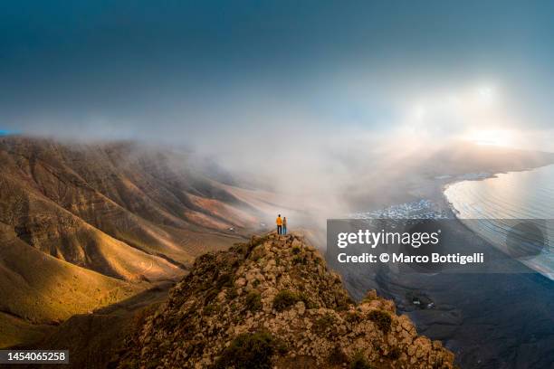 couple standing on top of a cliff looking at sunset, lanzarote, spain - majestic sky stock pictures, royalty-free photos & images