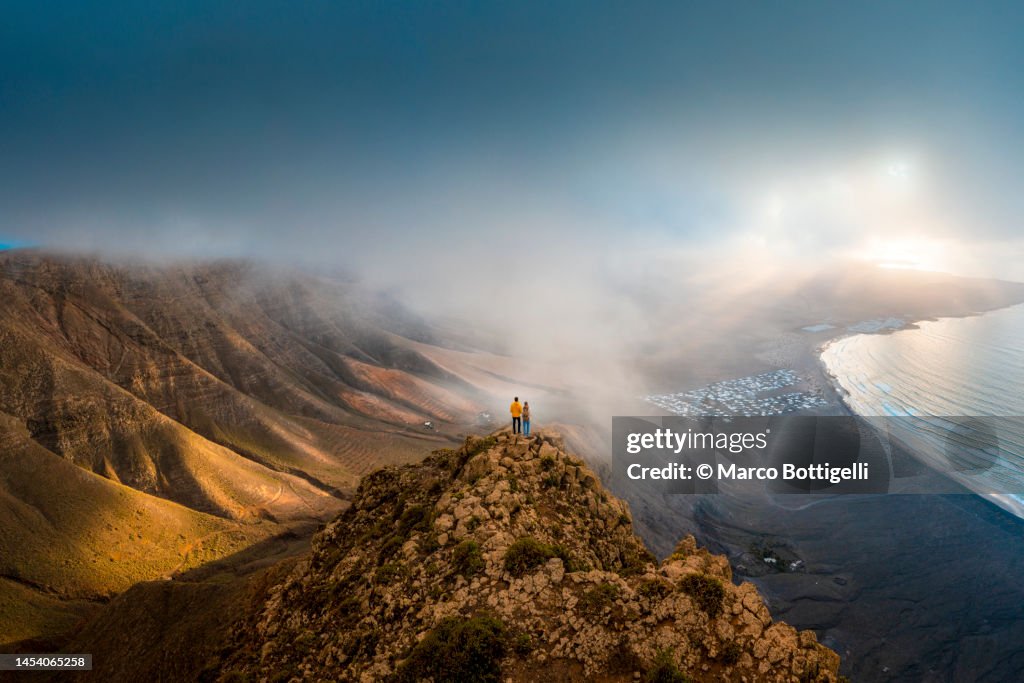 Couple standing on top of a cliff looking at sunset, Lanzarote, Spain
