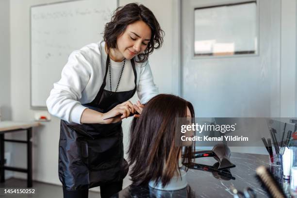 a student working as a hairdresser with a dummy - cabeleireiro imagens e fotografias de stock