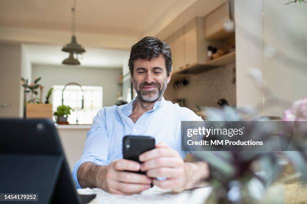 smiling man looking at smart phone at home - bearded man stock pictures, royalty-free photos & images