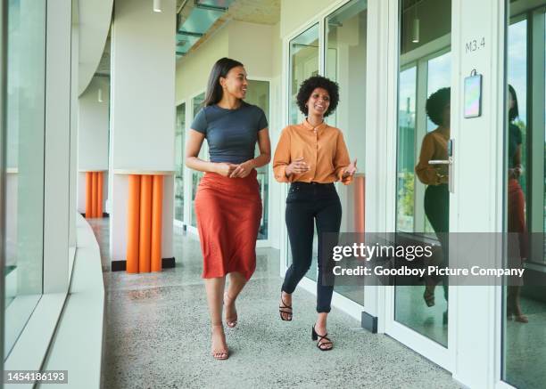 diverse young businesswomen talking while walking along an office hall - corporate modern office bright diverse imagens e fotografias de stock