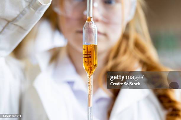 measuring an orange substance at school - pipet laboratoriumapparatuur stockfoto's en -beelden