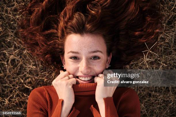 shy smiley woman lying on the grass of a park - hand on chin stock-fotos und bilder