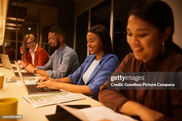 smiling businesspeople working around an office desk in the late evening - working side by side stock pictures, royalty-free photos & images