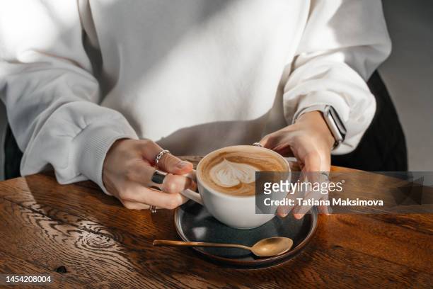 cappuccino in a white ceramic cup on a wooden table. close-up. - hand resting on wood stock-fotos und bilder