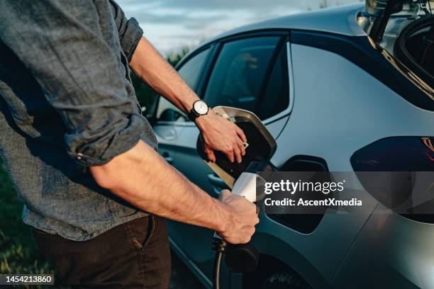 young man recharges electric vehicle - electric vehicle stock pictures, royalty-free photos & images
