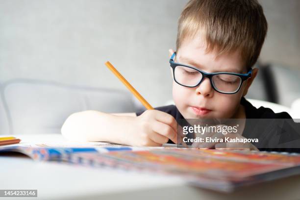 a boy of 8 years old in glasses draws with a colored pencil at the table at home, close up - 8 9 years foto e immagini stock