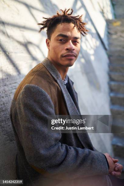 cool looking man looking off camera leaning against a wall - leben in der stadt stock-fotos und bilder