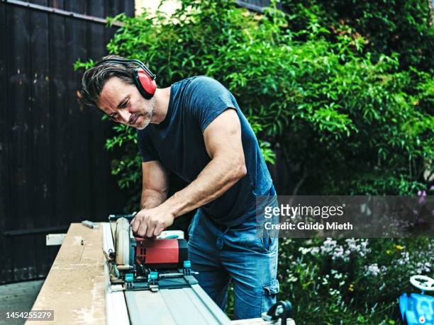 man using a saw and cutting piece of wood outdoor in garden. - electric saw stock pictures, royalty-free photos & images