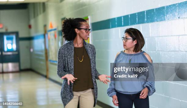 multiracial teachers converse, walking in school hallway - teachers talking stock pictures, royalty-free photos & images