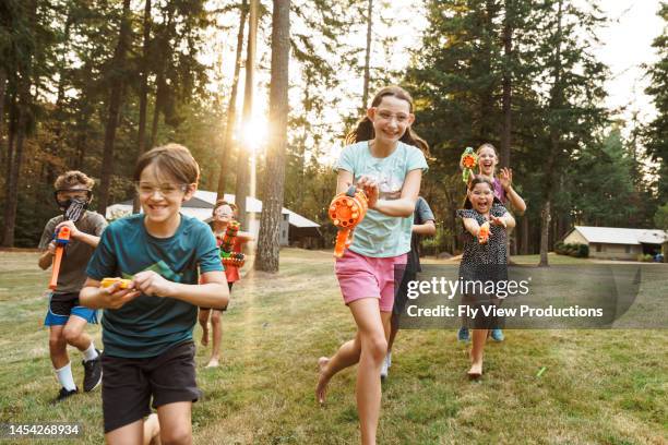 group of kids having a fun nerf gun battle outside - arma de brinquedo imagens e fotografias de stock