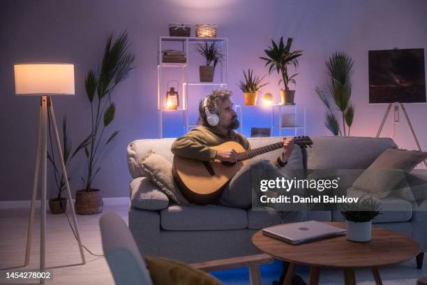 man with headphones playing the guitar at home. - etereo stock pictures, royalty-free photos & images