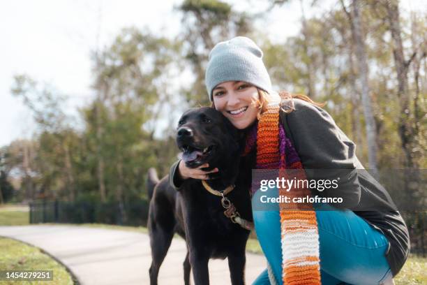 streichelhund während des spaziergangs - hundeliebe - spazierenhund in einem park - umarmung -schwarz / schokolade labrador - shawl collar stock-fotos und bilder