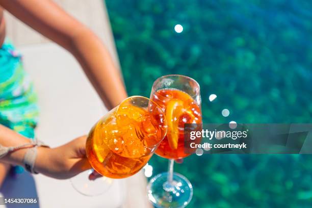 frauen stoßen mit einem s aperol spritz cocktail auf einem deck über dem ozean an. - tropischer cocktail stock-fotos und bilder