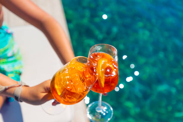 women toasting with a s spritz cocktail on a deck over the ocean. - orange cocktail stock pictures, royalty-free photos & images