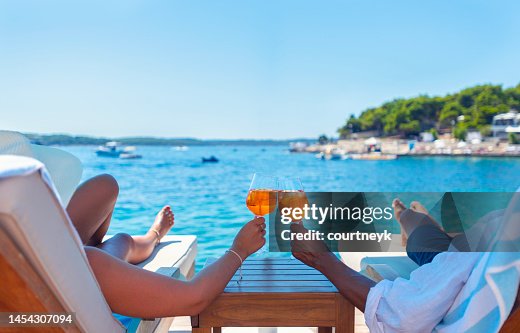 Couple relaxing and toasting with a Spritz cocktail on a beach deck over the ocean. Couple relaxing and toasting with a Spritz cocktail on a beach deck over the ocean.