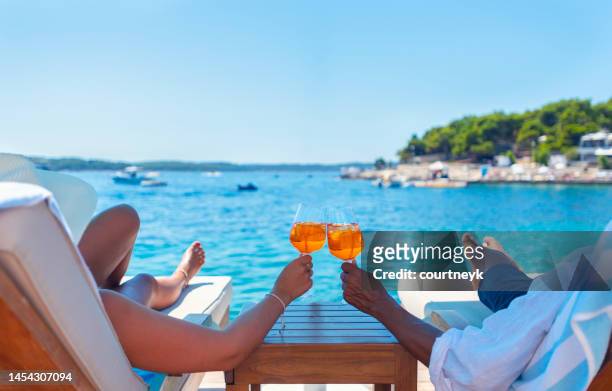 couple relaxing and toasting with a spritz cocktail on a beach deck over the ocean. - zonnestoel stockfoto's en -beelden