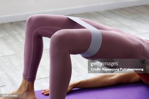 fitness concept. woman in sportswear training with elastic resistance band above knees in fitness studio or living room. lady doing glute bridge exercise for buttocks and legs - hips stock-fotos und bilder