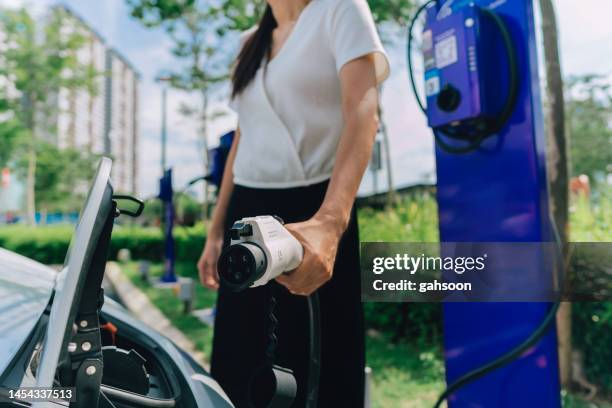 woman plugging cable to electric car. - sustainable transportation stock pictures, royalty-free photos & images