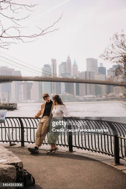 couple leaning on the railing in dumbo park with manhattan in the background - brooklyn bridge park fotografías e imágenes de stock