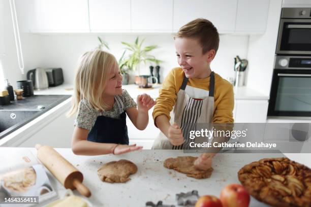 a brother and a sister laughing together as they preparing a apple pie in the kitchen - kids play apple photos et images de collection