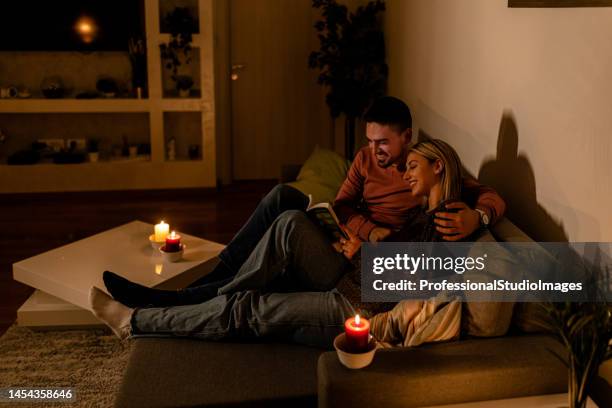 ein junges paar leidet zu hause unter einer stromkrise und liest bücher. - abenddämmerung stock-fotos und bilder