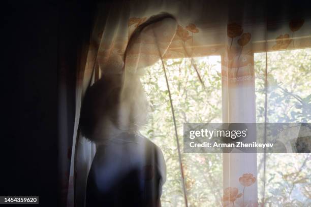 human wearing bunny head mask and standing at the window behind the curtain. 2023 is a rabbit zodiac sign. nicely fits for book cover - cinematic stock pictures, royalty-free photos & images