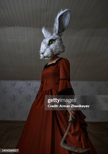 woman wearing bunny head mask and vintage victorian styled dress in a dark room holds sharp sickle. 2023 is a rabbit zodiac sign. nicely fits for book cover - easter mask stock-fotos und bilder