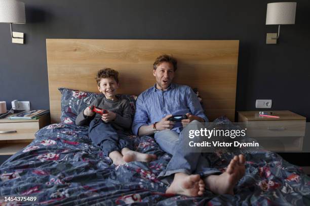 happy boy plays video game with his dad on the bed - padre soltero fotografías e imágenes de stock