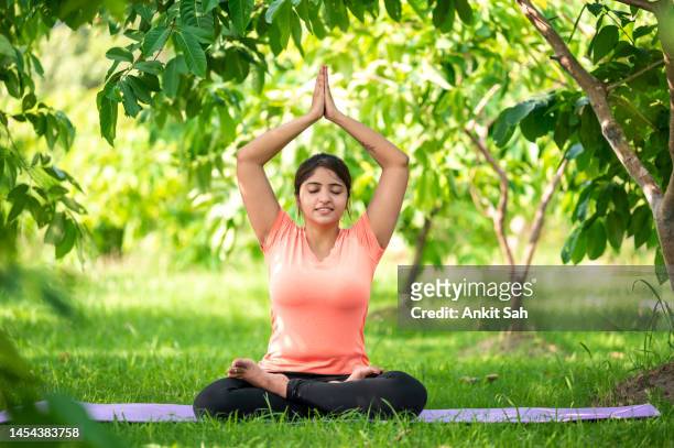 junge frau, die yoga und meditation in lotus-pose beim training im freien im park macht. - prayer pose greeting stock-fotos und bilder