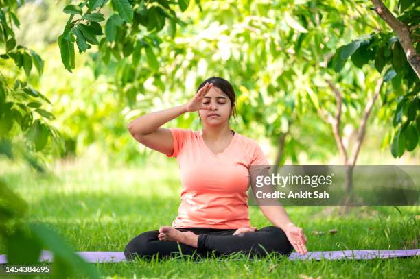 frau übt pranayama oder atemübungen, während sie in lotuspose sitzt - prayer pose greeting stock-fotos und bilder