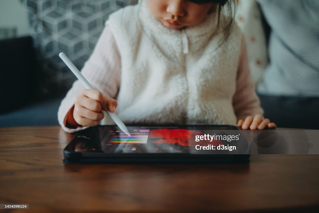 Cropped shot of a little Asian girl drawing on digital tablet using a digitized pen at home. Creative learning. Children's engagement of digital technology