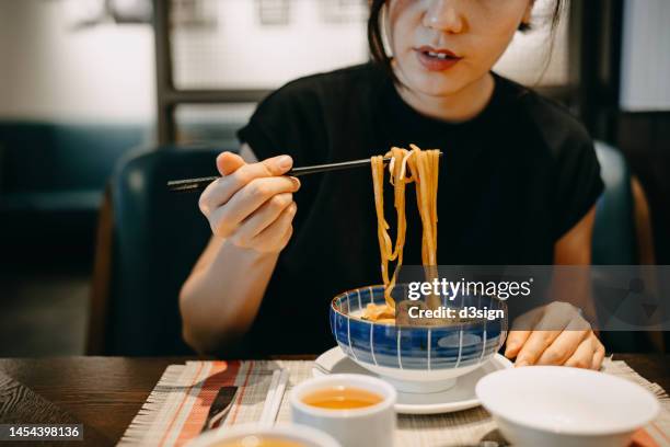 cropped shot of young asian woman enjoying a bowl of noodles, using chopsticks, with a cup of tea in a chinese restaurant - chinese food stock-fotos und bilder