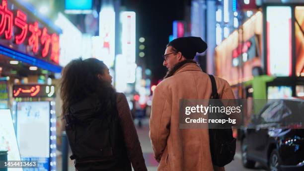multi-racial tourist friends walking in streets and exploring town in tokyo at night - billboards side by side stock pictures, royalty-free photos & images