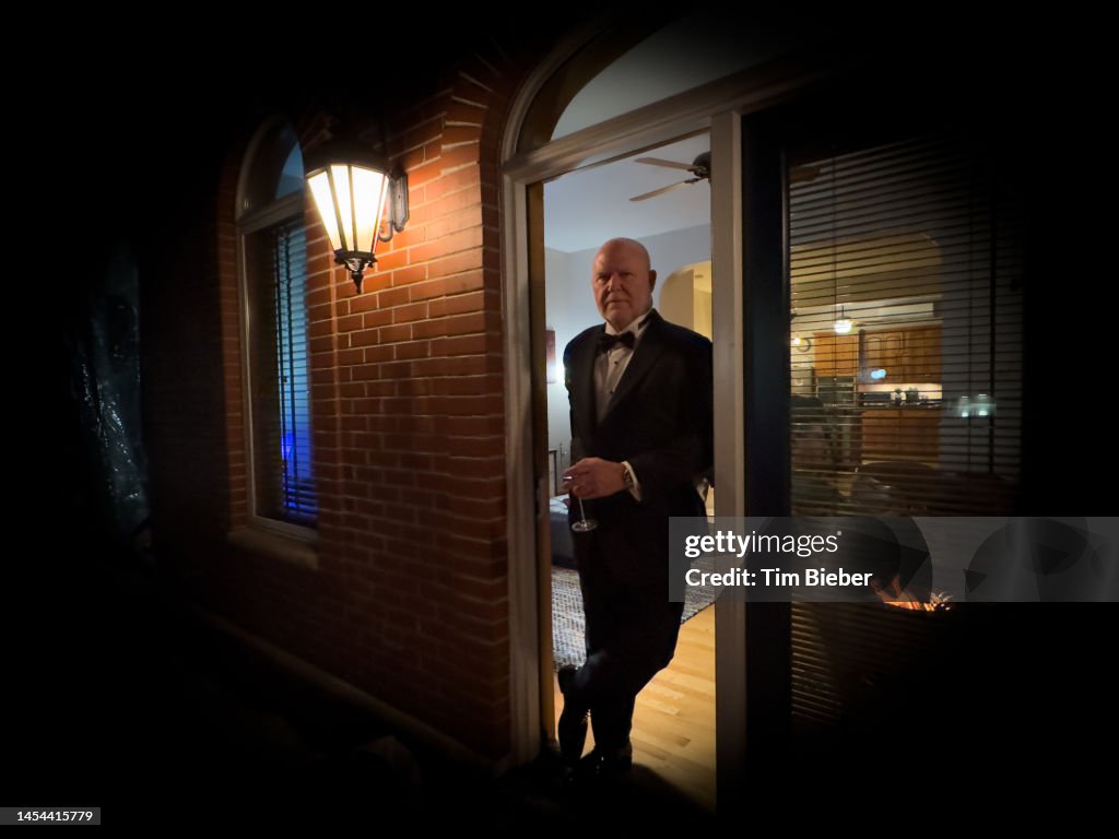 Man in tuxedo relaxing in doorway with drink.