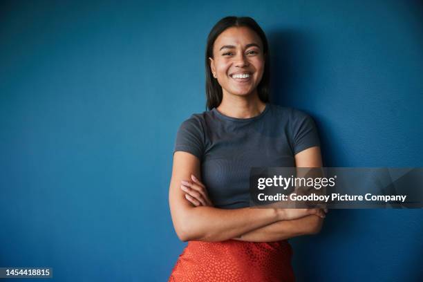 young businesswoman smiling while standing against a blue backdrop - colour background woman stock pictures, royalty-free photos & images