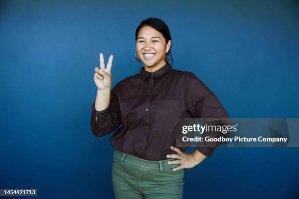 laughing businesswoman making a peace sign on a blue background - background color stock pictures, royalty-free photos & images