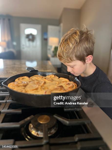 young boy looking at a pan of fresh baked cinnamon rolls - ijzer stockfoto's en -beelden
