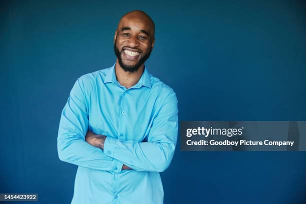 businessman laughing while standing with his arms crossed on a blue backdrop - background color stock pictures, royalty-free photos & images