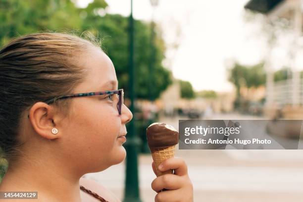 blonde girl with glasses eating an ice cream on a park. - child obesity stock pictures, royalty-free photos & images