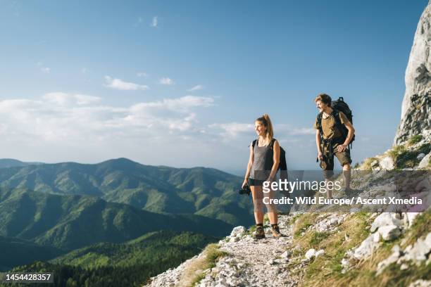 hiking couple pause on mountain slope above valley - escape rom stock pictures, royalty-free photos & images