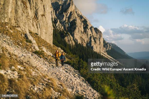 hikers ascend mountain slope above valley - escape rom stock pictures, royalty-free photos & images