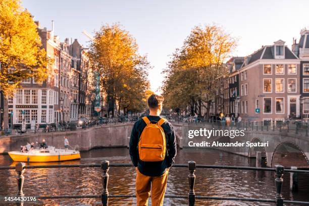 rear view of a man looking at amsterdam canal on a sunny day, netherlands - avventure di viaggio foto e immagini stock