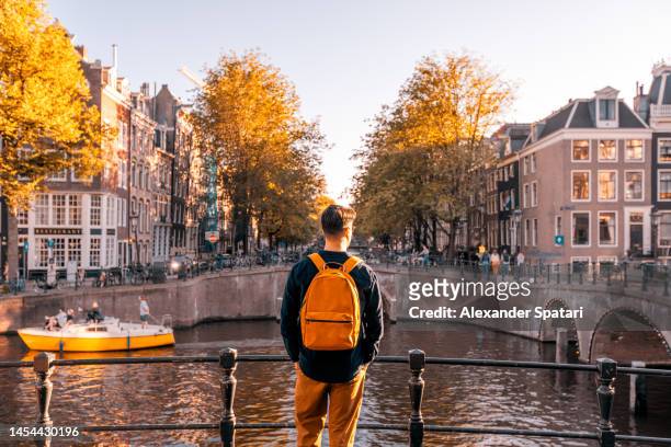 rear view of a man looking at amsterdam canal on a sunny day, netherlands - europa geografische locatie stockfoto's en -beelden