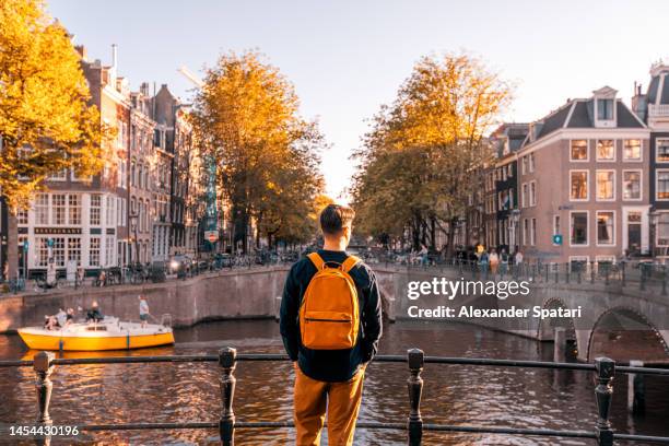 rear view of a man looking at amsterdam canal on a sunny day, netherlands - solo travel backpack stock pictures, royalty-free photos & images