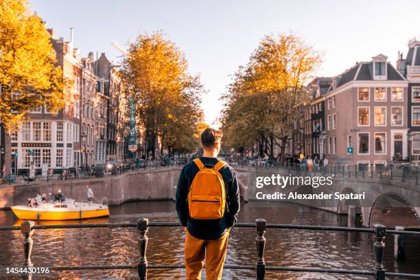 rear view of a man looking at amsterdam canal on a sunny day, netherlands - tourist in city stock pictures, royalty-free photos & images