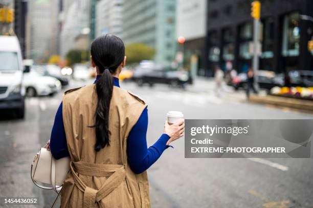 businesswoman seen from behind on the street of new york during her coffee break - beige purse stockfoto's en -beelden